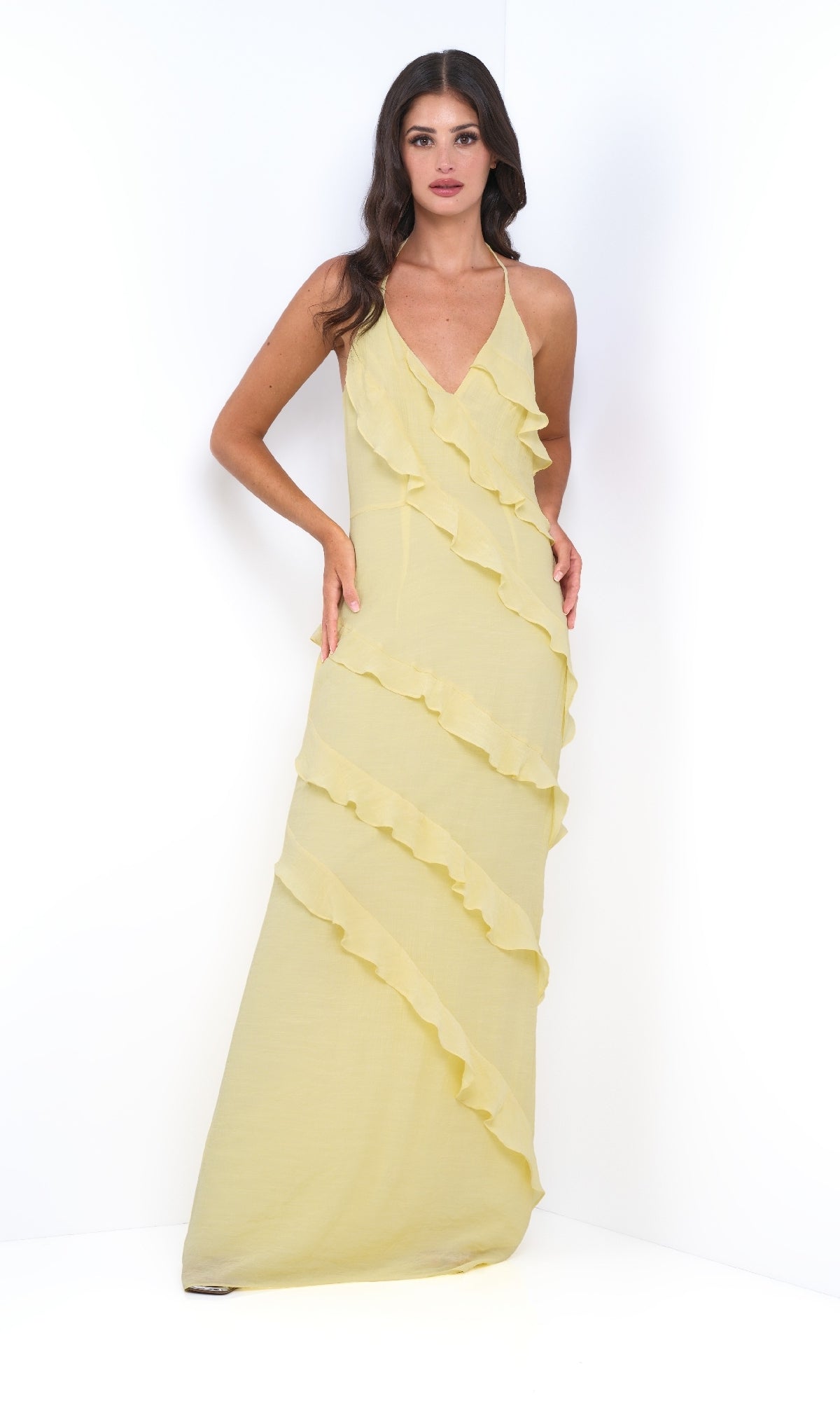 A woman stands against a white background wearing the Remi by Velvi V-Neck Halter Ruffled Long Prom Dress in yellow, featuring diagonal ruffle details and a sleeveless design.